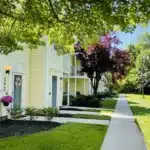 A row of yellow townhouses with manicured lawns and a tree-lined sidewalk on a sunny day.