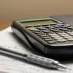 A calculator resting on a stack of papers with handwritten notes, alongside a blue-tipped pen.